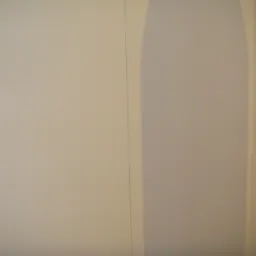 Wnętrze po świeżym malowaniu, widoczna ściana w beżowym odcieniu z subtelnym cieniem wzdłuż krawędzi, sugerującym narożnik lub załamanie powierzchni.