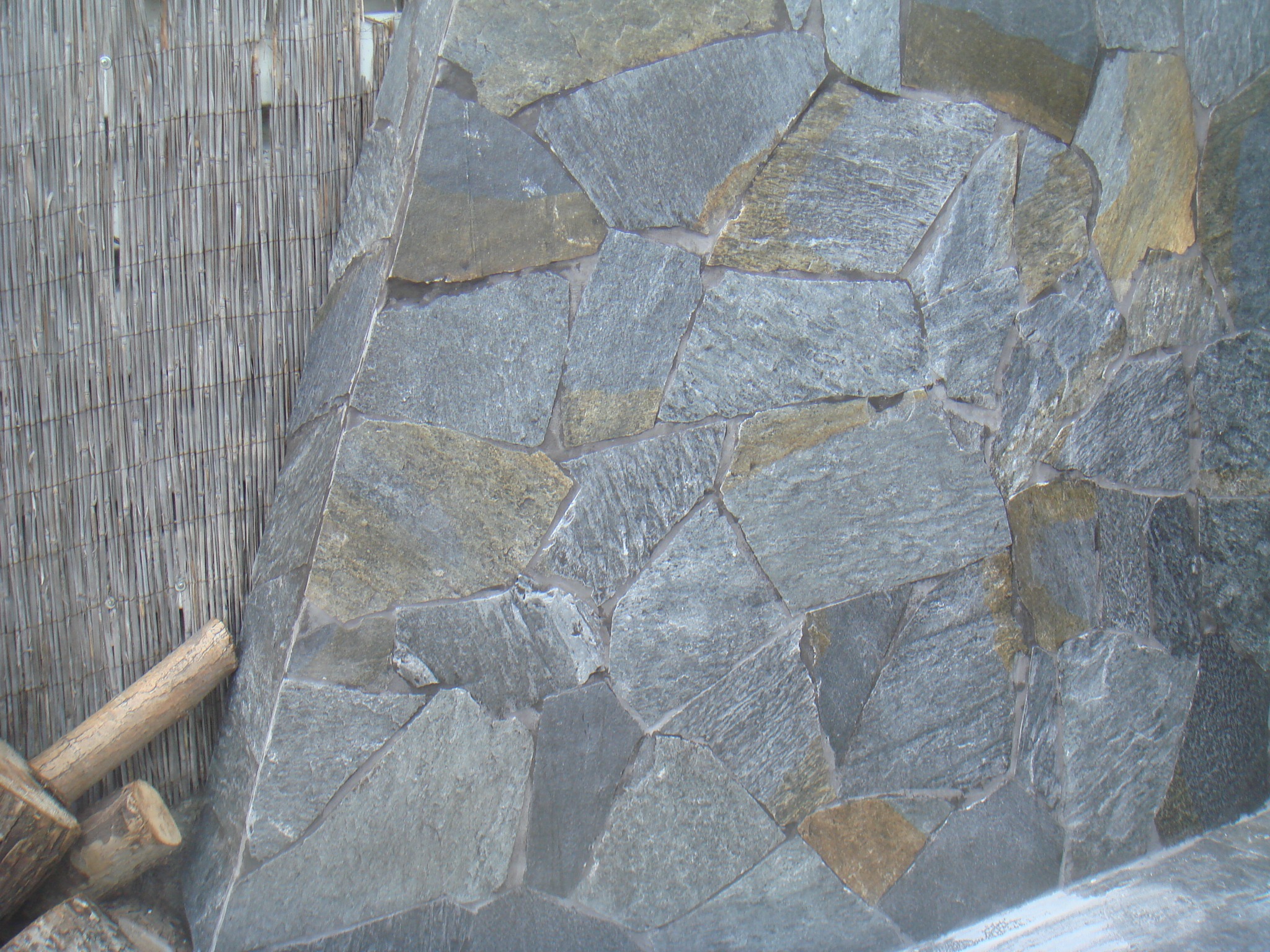 Szara elewacja z nieregularnych kamieni, widoczna obok bambusowej maty i drewna, wykonana w Bydgoszczy.