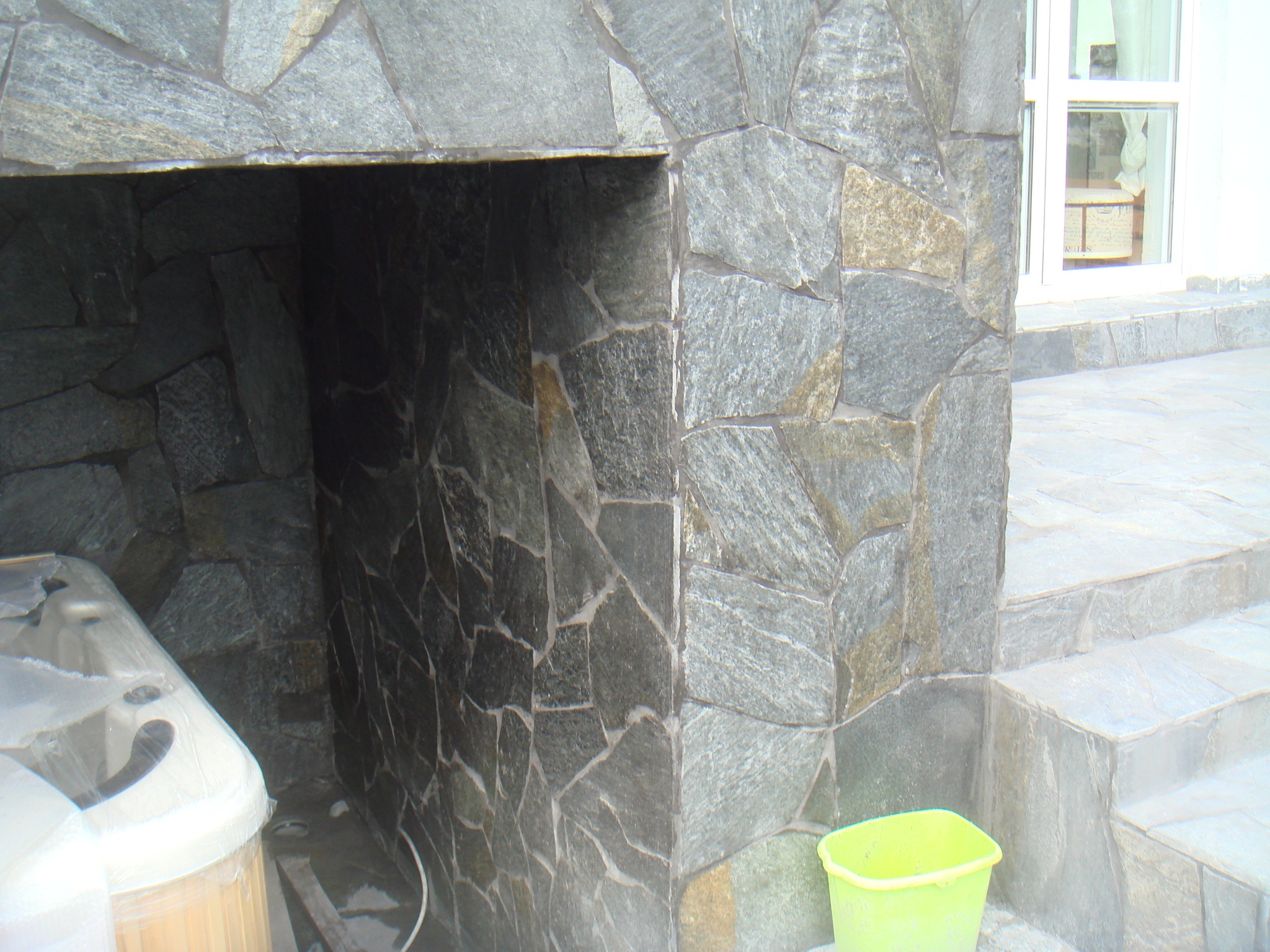 Kamienna elewacja zewnętrzna z wnęką, obok schody i wiadro, widoczna wanna w folii.