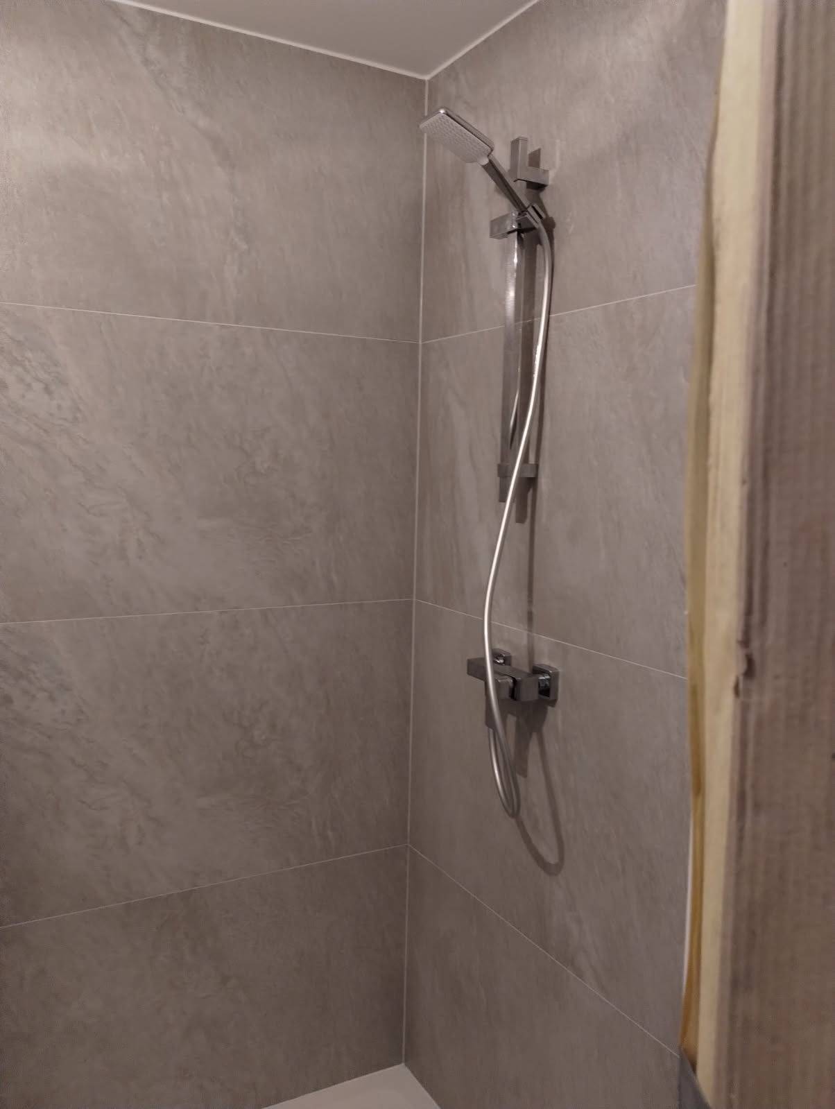 Wykończona kabina prysznicowa z szarymi, marmurkowymi płytkami i nowoczesną armaturą, ukazana w ciepłym oświetleniu z bliska.