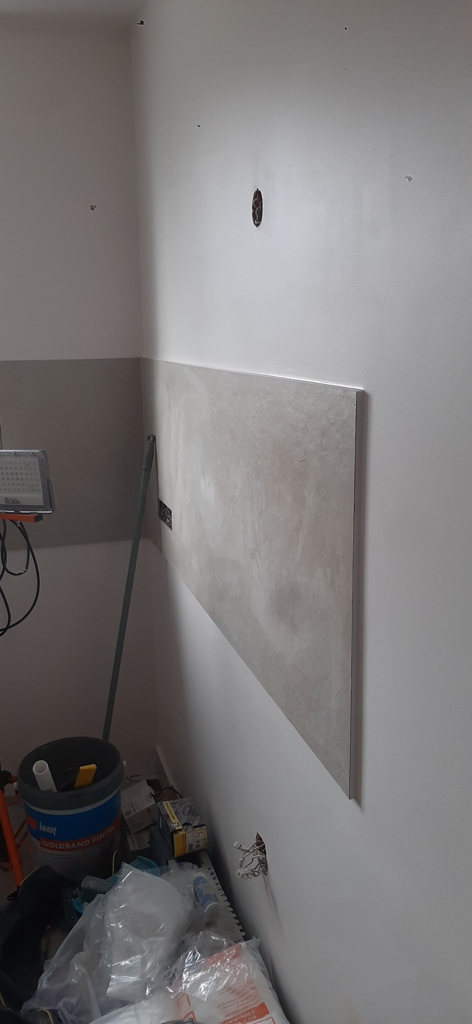 Fragment ściany z zamontowaną płytą imitującą kamień, widoczne narzędzia i materiały budowlane. Częściowo wykończone wnętrze w trakcie prac.