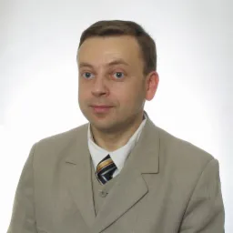 Portret mężczyzny w beżowym garniturze i krawacie w paski na jasnym tle.