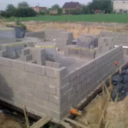 Wznoszenie ścian fundamentowych z bloczków betonowych na budowie domu jednorodzinnego. Ujęcie z bliska, widoczne bloczki i teren budowy.