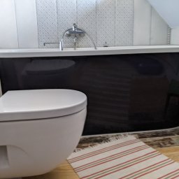 Wett - Biała toaleta z widoczną czarną wanną na tle płytek w łazience, mały zielony stołek dziecięcy w rogu.