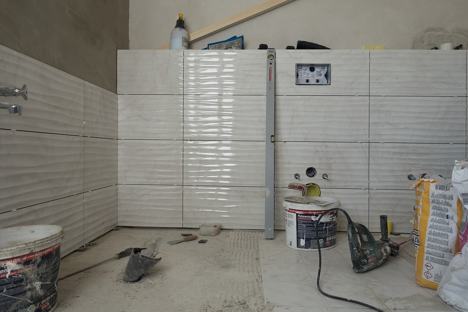 Proces układania płytek o falistej strukturze w łazience, widoczny poziomica, puszka instalacyjna i narzędzia.