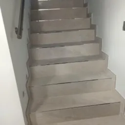 Schody wewnętrzne wyłożone płytkami imitującymi marmur, z metalowymi listwami na krawędziach, ujęcie z dołu.