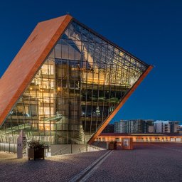 Fotografia Radosław Dybała - Nowoczesny budynek o nietypowej architekturze z elementami szkła i cegły, oświetlony nocą, z widocznymi detalami elewacji i otoczenia.