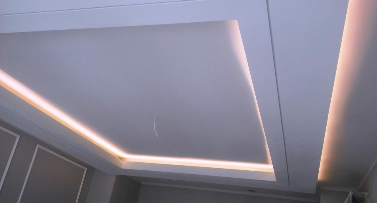 Sufit podwieszany z oświetleniem LED wzdłuż krawędzi, widok z dołu, z widocznym fragmentem ściany z dekoracyjną sztukaterią.