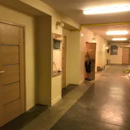 Korytarz z nowo zamontowanymi, drewnianymi drzwiami wewnętrznymi z poziomymi przeszkleniami, widoczne elementy wykończeniowe i osoba w tle.