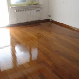 Błyszcząca, świeżo polakierowana podłoga z parkietu w odcieniach brązu, odbijająca światło z okna, widoczny biały grzejnik pod oknem i listwy przypodłogowe.