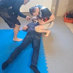 Szkoła Ochrony Kurs Ochrony STS Security Tactical Services Skierniewice - Symulacja zatrzymania osoby z użyciem kajdanek podczas szkolenia z zakresu bezpieczeństwa. Instruktorzy demonstrują techniki interwencji na macie.