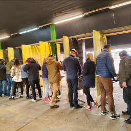 Szkoła Ochrony Kurs Ochrony STS Security Tactical Services Skierniewice - Strzelnica: grupa osób w ochronnikach słuchu, uczestniczących w zajęciach strzeleckich. Widoczne stanowiska z żółtymi przegrodami i liczne łuski na podłodze.