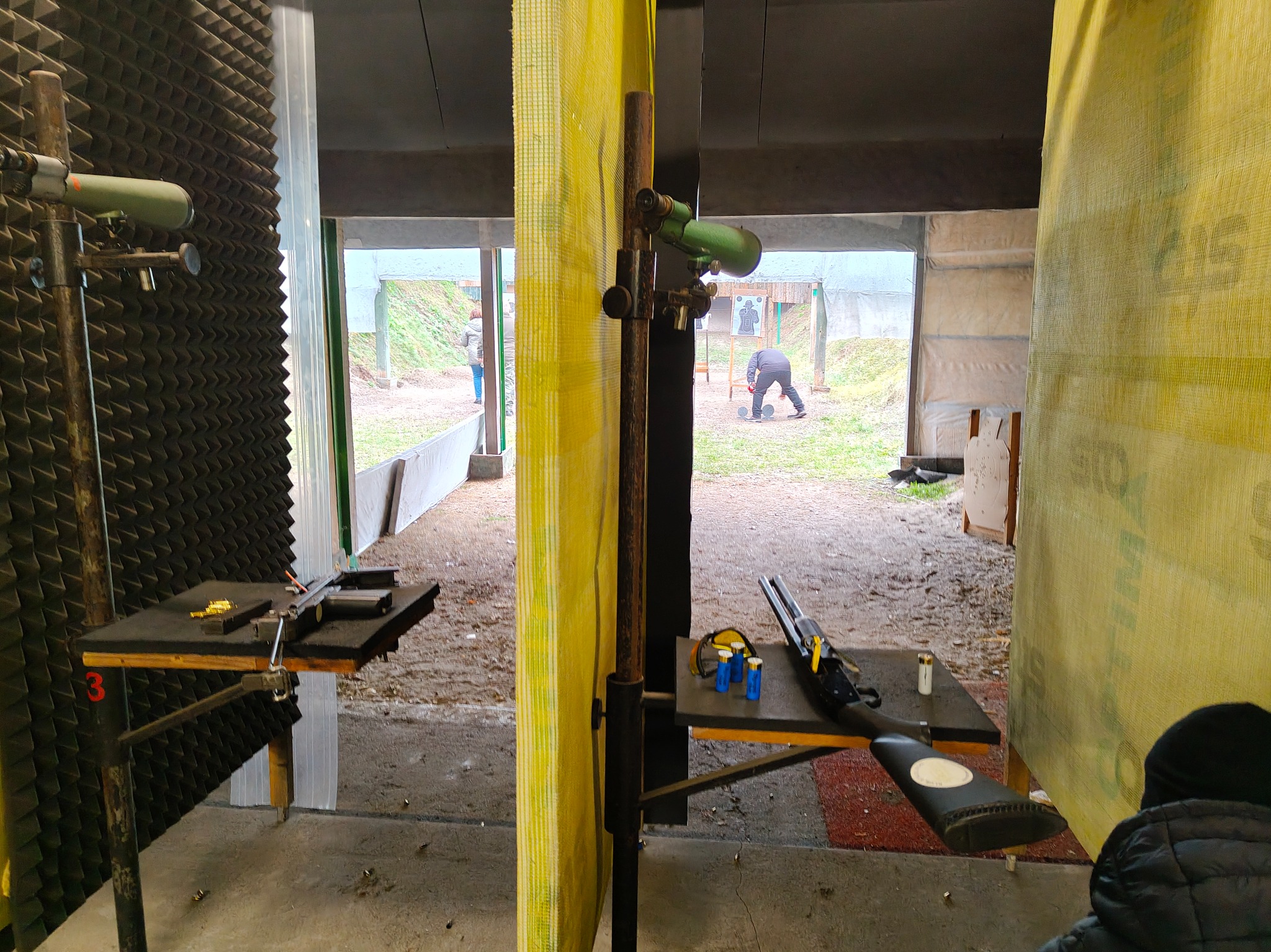 Strzelnica z bronią na stole, widok przez stanowisko strzeleckie na osobę sprawdzającą tarczę. Akustyczne panele na ścianach. Trening strzelecki.