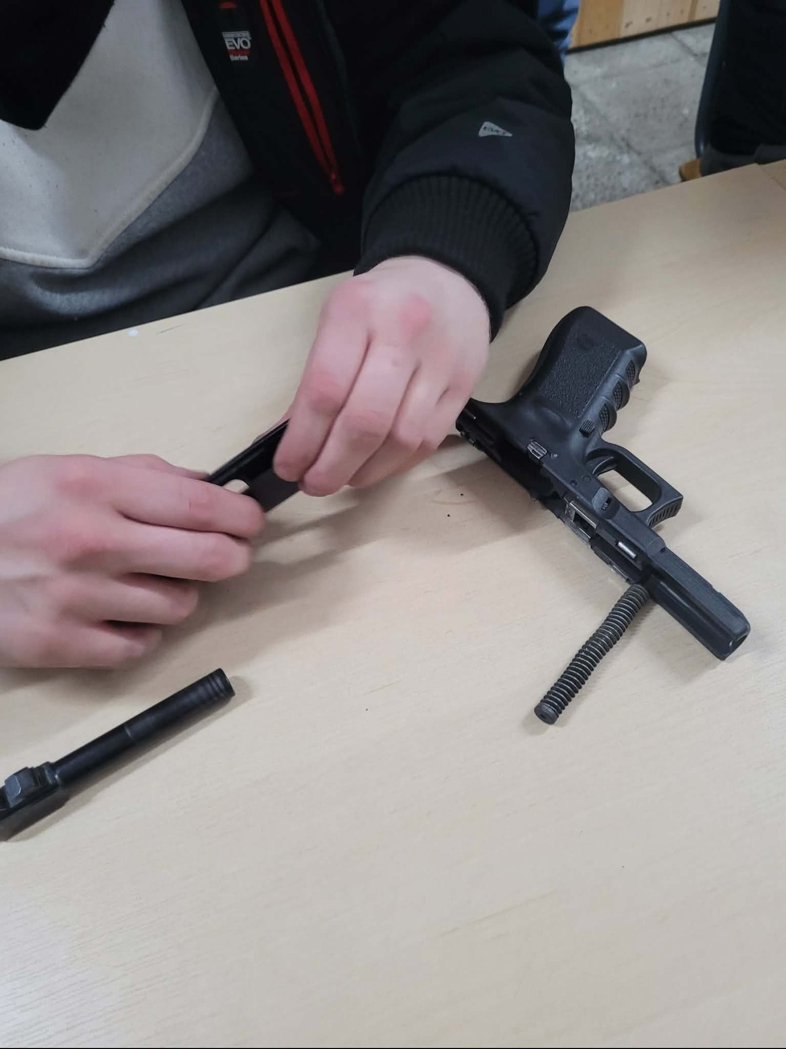 Rozkładanie pistoletu Glock na stole podczas szkolenia w Skierniewicach. Widoczne elementy broni i dłonie osoby wykonującej czynność.