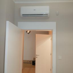 KLIMA-KURP - Zamontowany klimatyzator Haier na ścianie nad otwartymi drzwiami w jasnym pomieszczeniu z parkietem, widoczny czujnik ruchu i włącznik światła.