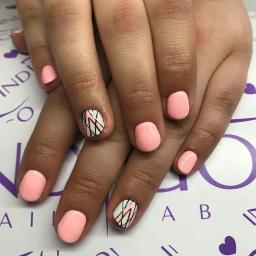 Bellezza Salon Fryzjersko-Kosmetyczny - Dłonie z pomalowanymi na jasny różowo paznokciami, jeden paznokieć z geometrycznym wzorem w czerni i bieli, na tle z logo Indigo.