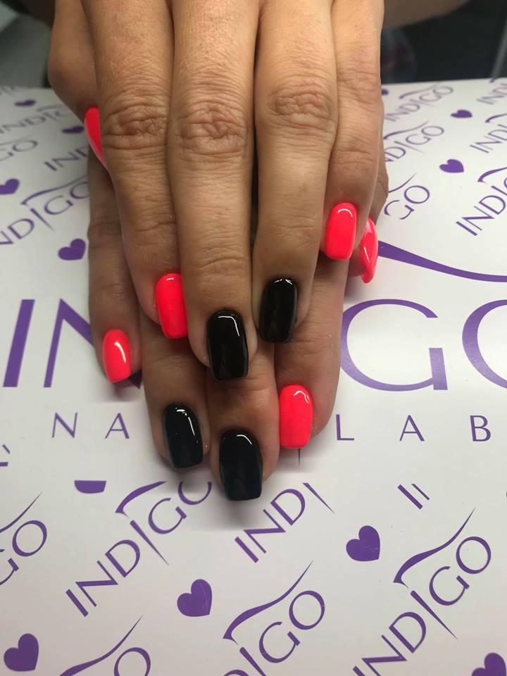 Dłonie z pomalowanymi paznokciami w kolorze neonowej czerwieni i czerni na tle z logo Indigo.