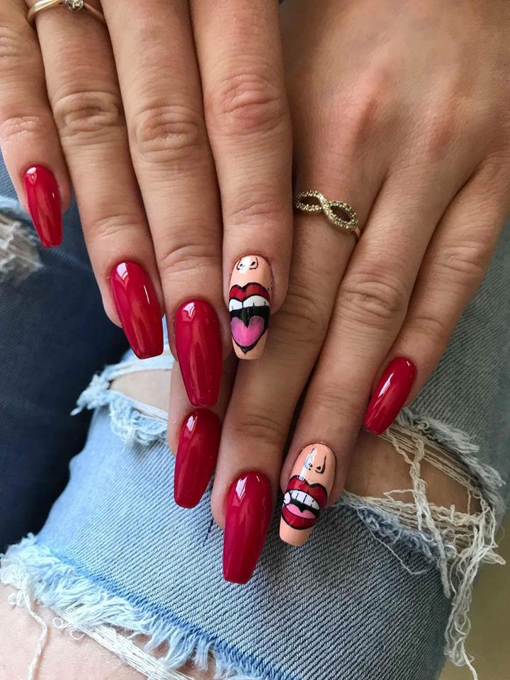 Dłonie z czerwonymi, błyszczącymi paznokciami w kształcie migdała i paznokciami z artystycznym zdobieniem ust z sercem, na tle podartych jeansów.