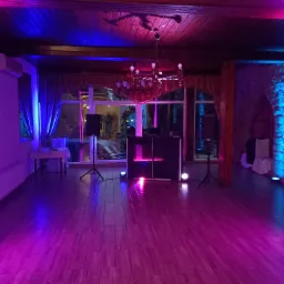 Sala bankietowa z parkietem i DJ-ką oświetlona niebiesko-różowymi światłami. Widoczny żyrandol i kolumny.