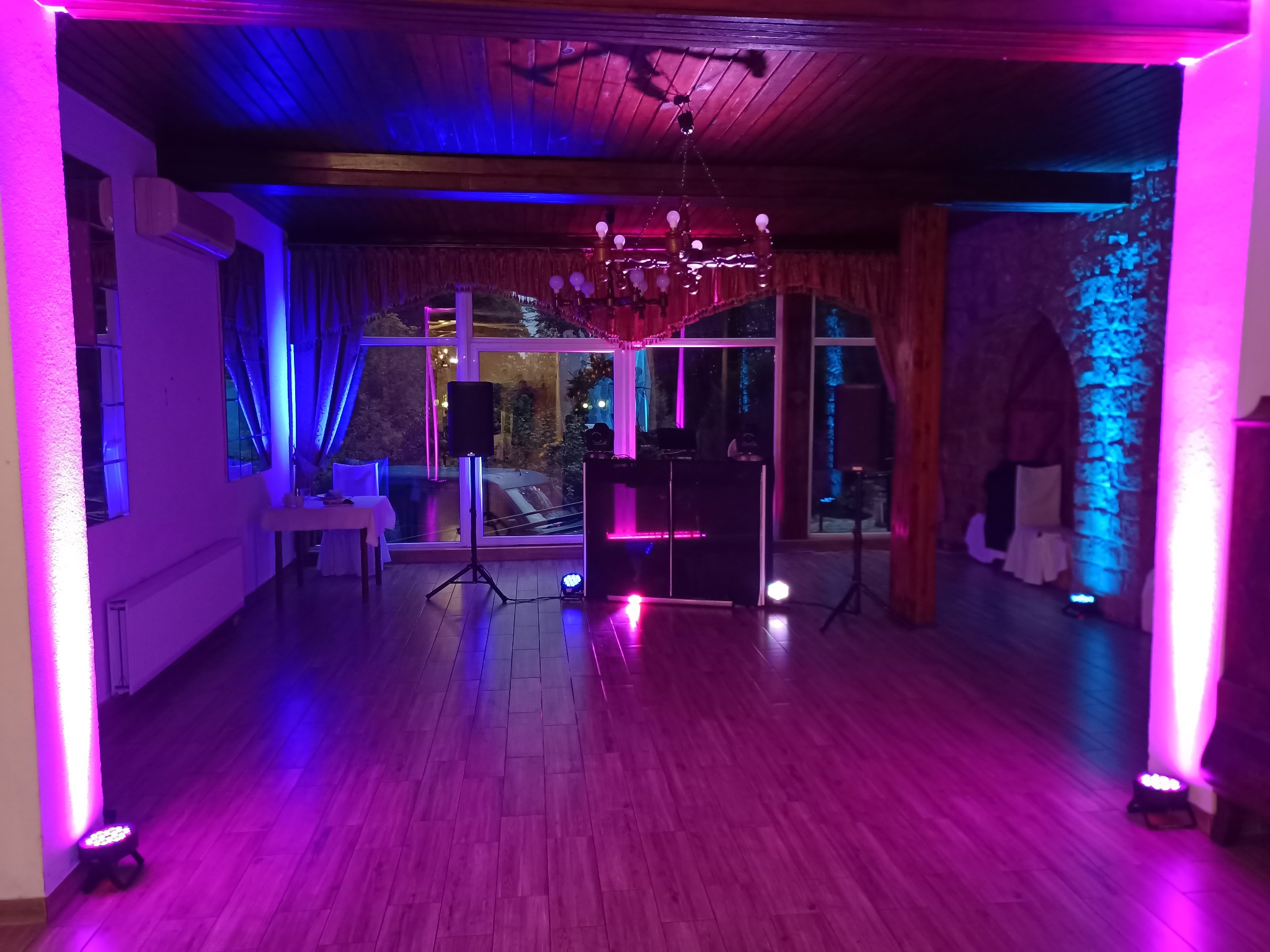 Sala bankietowa z parkietem i DJ-ką oświetlona niebiesko-różowymi światłami. Widoczny żyrandol i kolumny.
