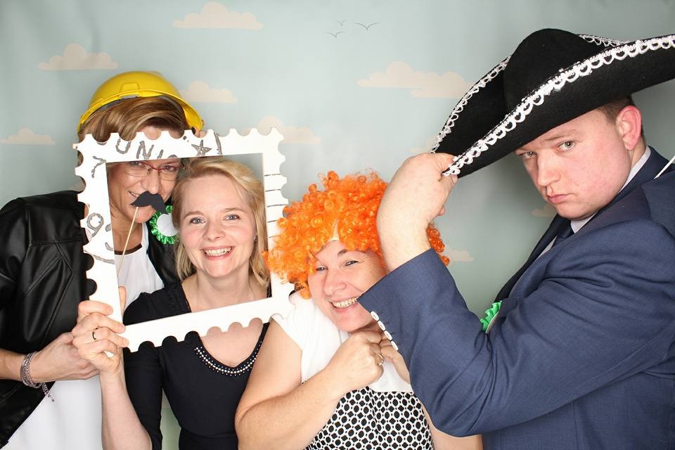 Wesoła sesja zdjęciowa z rekwizytami: cztery osoby w przebraniach, w tym kapelusz meksykański i peruka. Uśmiechnięte twarze i dekoracje na tle w chmurki.