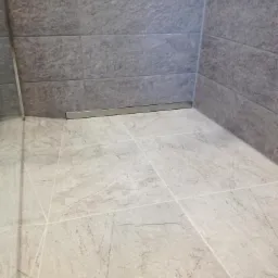 Wykończony odpływ liniowy w kabinie prysznicowej wyłożonej szarymi płytkami imitującymi kamień.