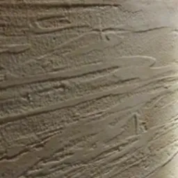 Tekstura ściany z wyraźnymi, poziomymi żłobieniami w odcieniach beżu i brązu, oświetlona z boku, tworząca efekt trójwymiarowości.