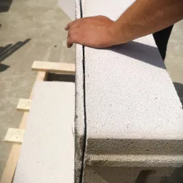 Układanie bloczków z betonu komórkowego na zaprawie cienkowarstwowej, widoczna ręka pracownika dociskająca element.
