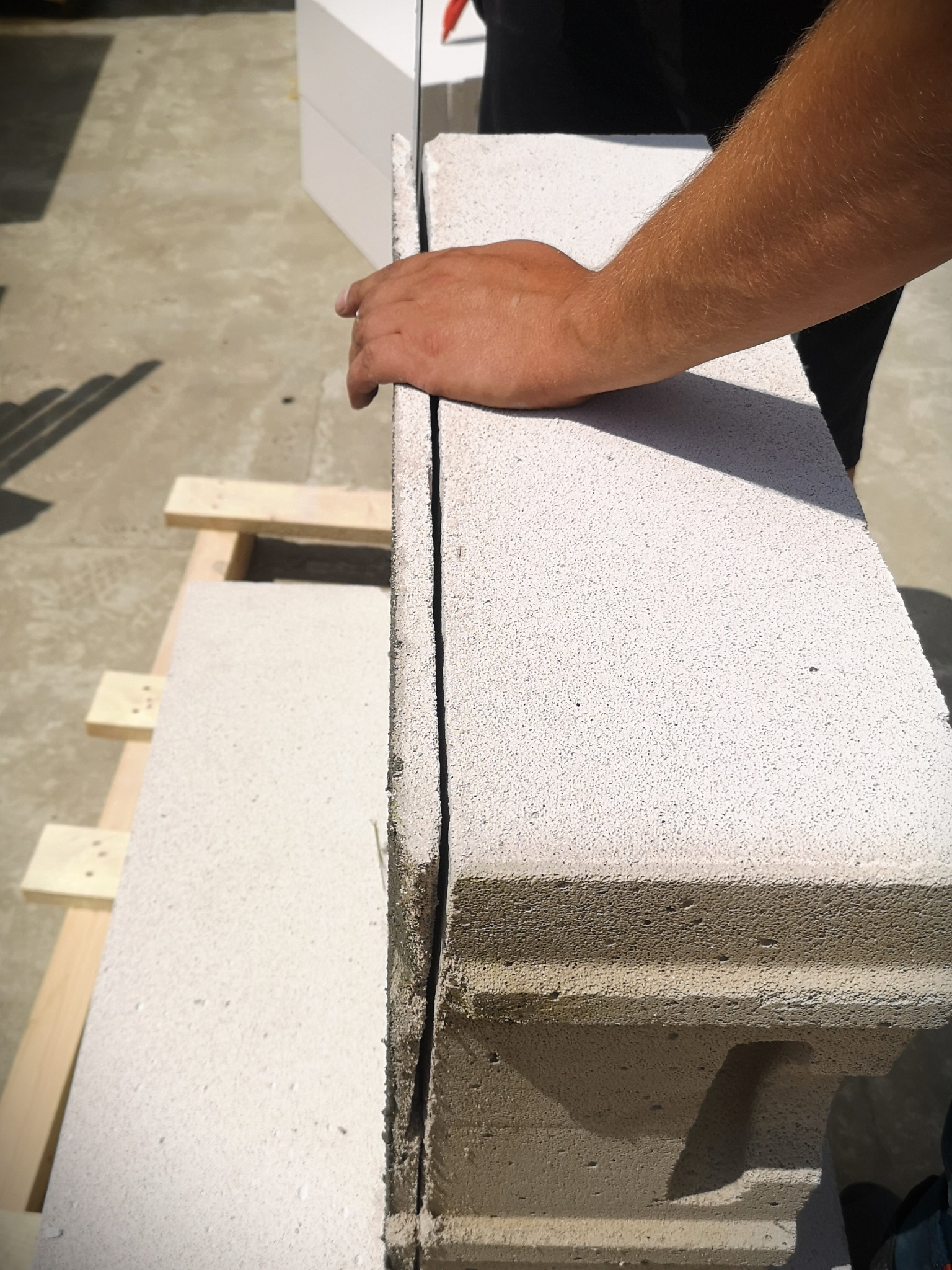 Układanie bloczków z betonu komórkowego na zaprawie cienkowarstwowej, widoczna ręka pracownika dociskająca element.