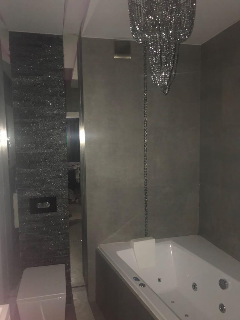 Szara łazienka z wanną z hydromasażem, brokatową ścianą i kryształowym żyrandolem