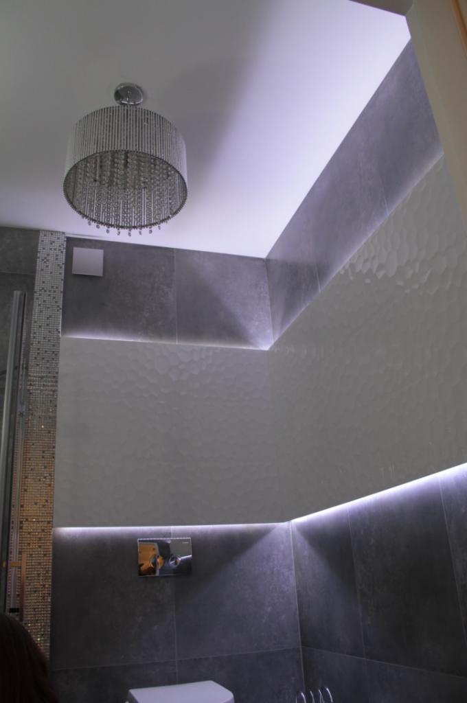 Nowoczesna łazienka z szarymi płytkami, dekoracyjnym oświetleniem LED i kryształowym żyrandolem, widok z dołu.