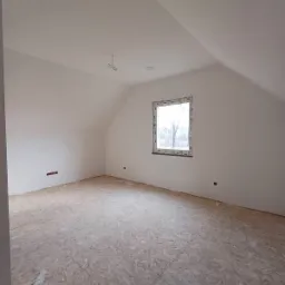 Poddasze z oknem dachowym po wykonaniu gładzi, widoczne przygotowane podłoże pod posadzkę, wystające kable elektryczne i puszka instalacyjna.