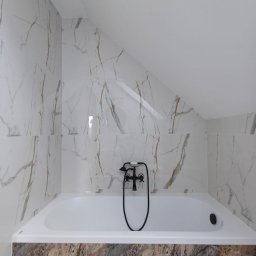 Usługi remontowo - budowlane Zbigniew Rzepka - Wykończona łazienka na poddaszu z białą wanną, baterią w stylu retro i marmurowymi płytkami na ścianach, z widocznym skosem sufitu.