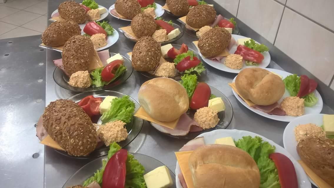 Przygotowane porcje kanapek na talerzach z dodatkami: sałata, papryka, pasta jajeczna i masło, ułożone na metalowym stole, gotowe do serwowania.