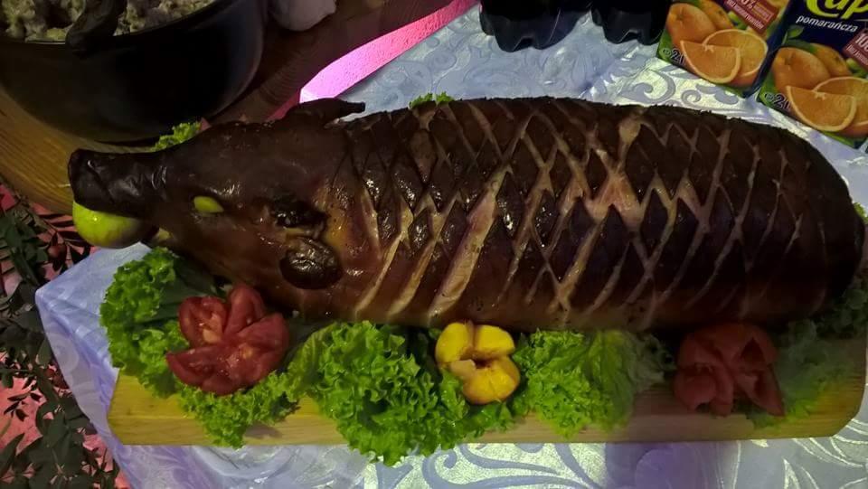 Pieczone prosię z jabłkiem w pysku, dekorowane sałatą, pomidorami i morelami na drewnianej desce, gotowe do serwowania.