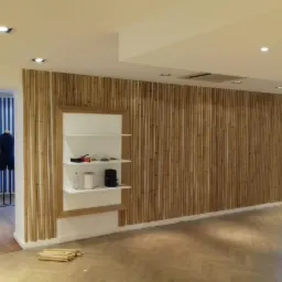 Ściana wykończona pionowymi listwami z drewna, z wkomponowanymi półkami, w jasnym wnętrzu sklepu z parkietem na podłodze i manekinami w tle.