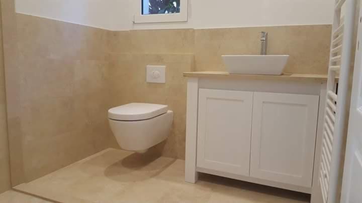 Jasna łazienka z beżowymi płytkami, podwieszana toaleta, biała szafka pod umywalką i grzejnik drabinkowy, minimalistyczny design.