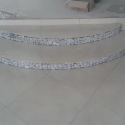 Dwa półokrągłe stopnie schodów wykończone mozaiką z białych kamieni, na podłodze jasne płytki. Widok z góry, ukończone prace.