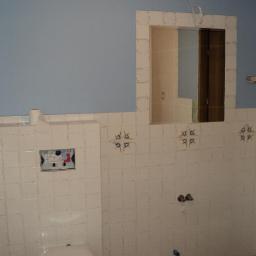 Marcin Ważydrąg - Błękitna ściana nad białymi, kwadratowymi płytkami w łazience. Widoczne przygotowania do montażu armatury i lustra. Charakterystyczny wzór na fugach płytek.