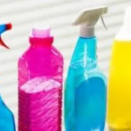 Różnokolorowe butelki z płynami do czyszczenia z rozpylaczami i dozownikami, ustawione obok siebie na jasnym tle.