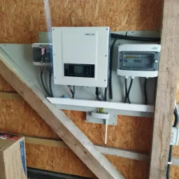 Zamontowany inwerter SOFAR wraz z zabezpieczeniami i skrzynką rozdzielczą na ścianie z boazerii, widoczne drewniane elementy konstrukcyjne budynku.