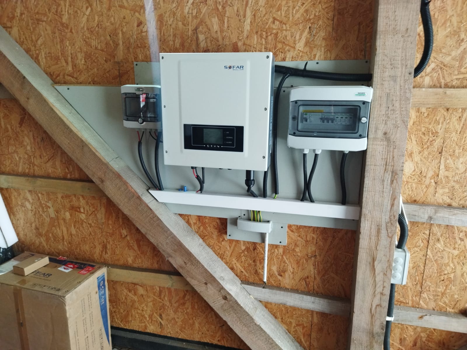Zamontowany inwerter SOFAR wraz z zabezpieczeniami i skrzynką rozdzielczą na ścianie z boazerii, widoczne drewniane elementy konstrukcyjne budynku.