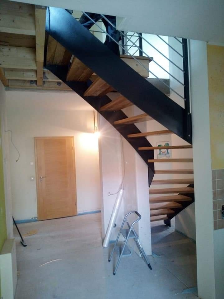 Wnętrze z drewniano-metalowymi schodami o konstrukcji wspornikowej, widoczne ślady prac wykończeniowych, drabina aluminiowa i folia ochronna na podłodze.