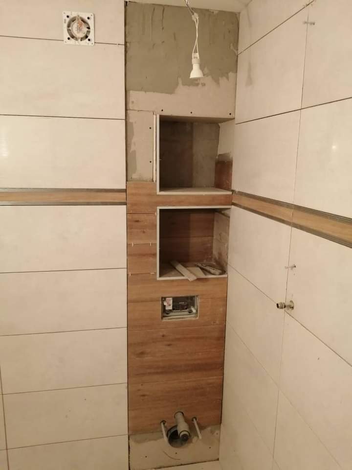 W trakcie realizacji remontu łazienki w Kraśniku: montaż drewnopodobnych płytek na ścianie z wnękami, widoczne elementy instalacji hydraulicznej i elektrycznej.