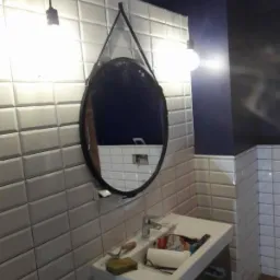 Łazienka po remoncie z białą, wypukłą glazurą ułożoną w cegiełkę, owalne lustro na pasku, biała umywalka z baterią, widoczne narzędzia i materiały budowlane.