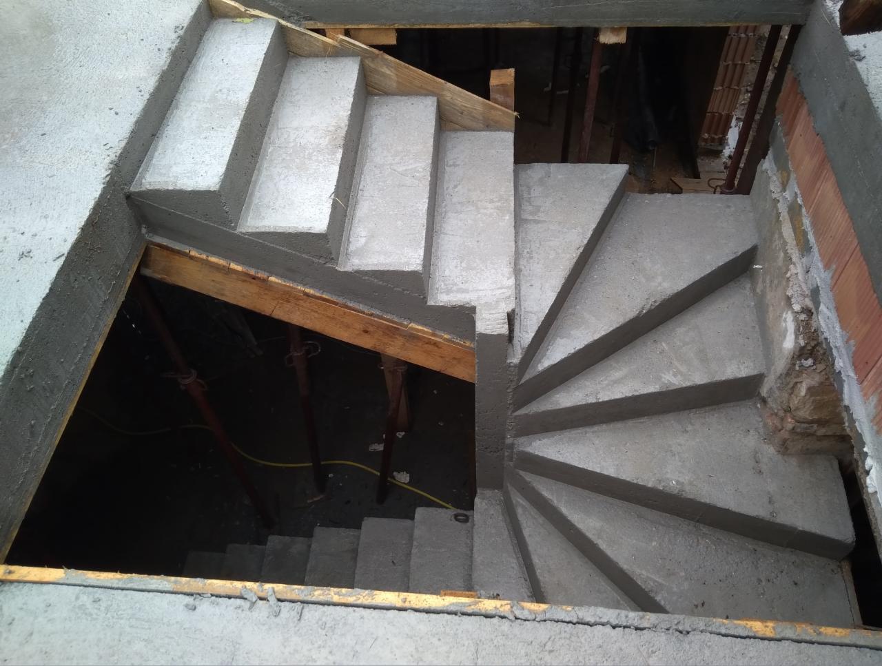 Wewnętrzne betonowe schody spiralne w surowym stanie, widok z góry, z widocznym deskowaniem i podporami, etap budowy.