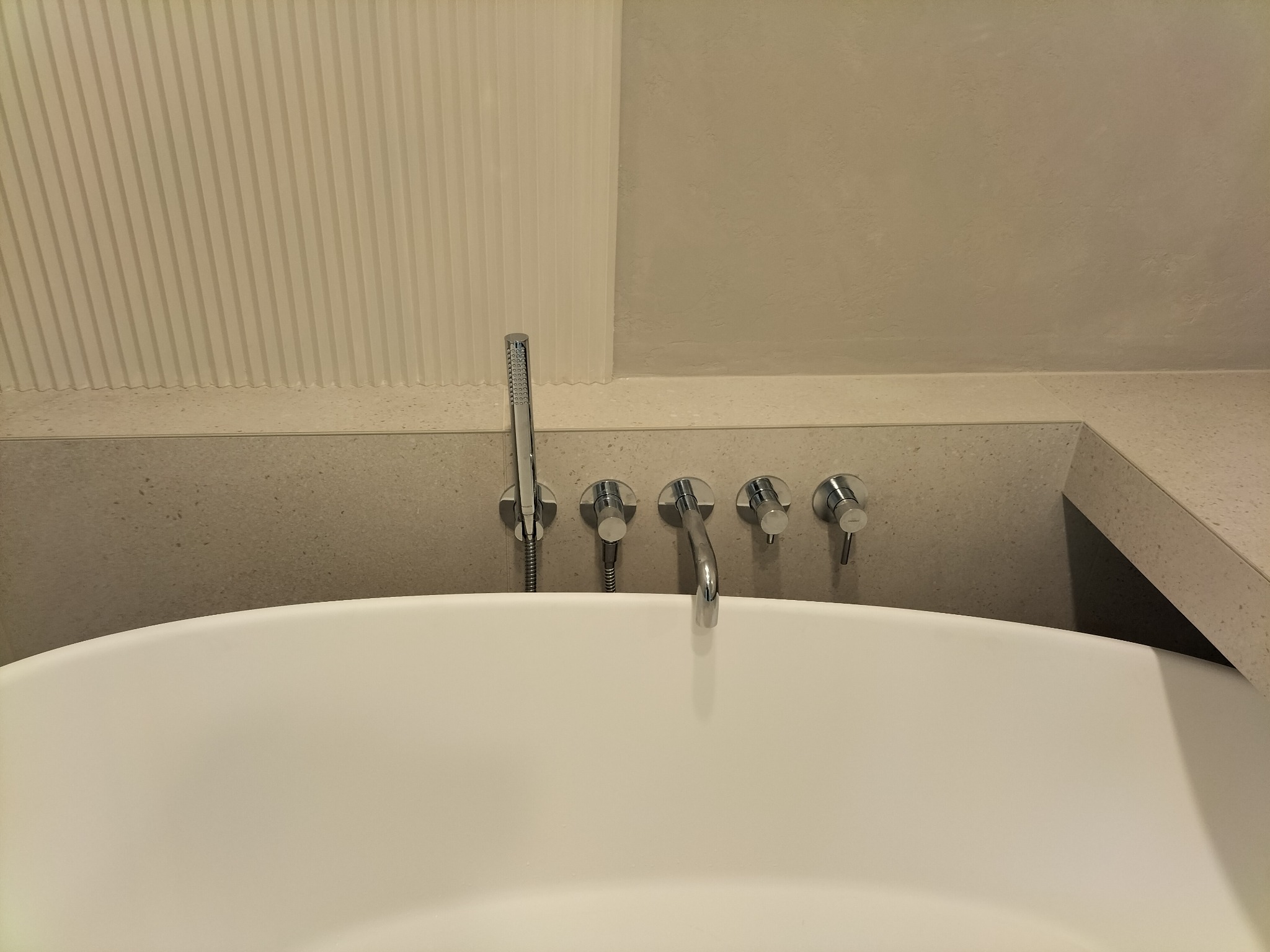 Nowoczesna, biała wanna wolnostojąca z chromowaną armaturą ścienną i panelem dekoracyjnym w tle, tworząca elegancki detal wykończenia łazienki.