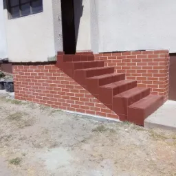 Wykończone klinkierem schody wejściowe do budynku, z widocznymi fugami i fragmentem elewacji.