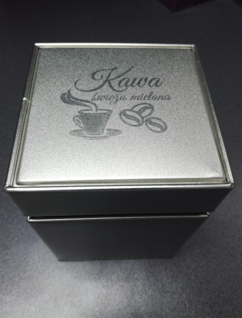 Metalowe pudełko kwadratowe z grawerowanym napisem 'Kawa świeżo mielona' oraz rysunkiem filiżanki i ziaren kawy.