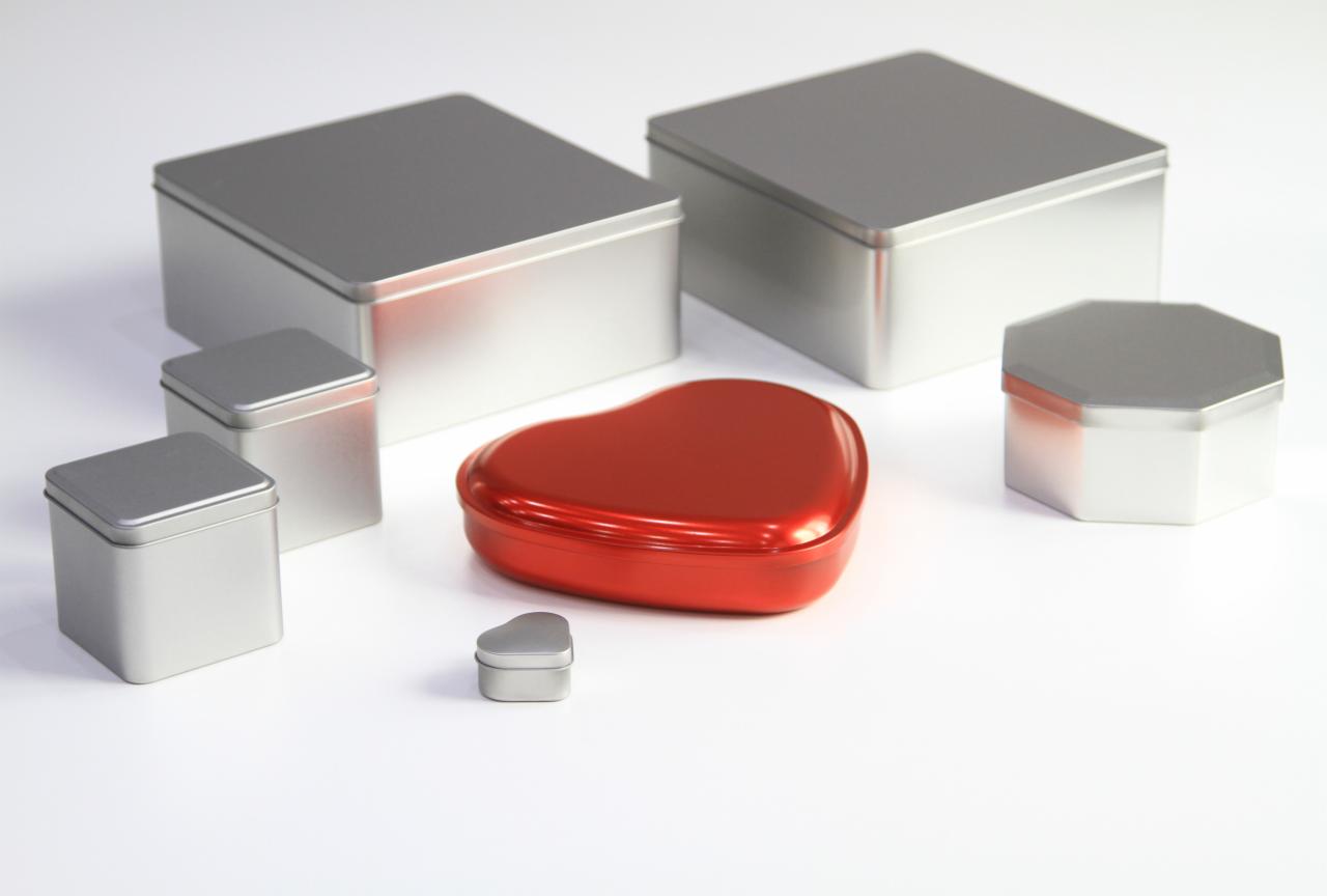 Zestaw metalowych pudełek o różnych kształtach: dwa duże kwadratowe, dwa małe kwadratowe, jeden mały w kształcie serca w kolorze czerwonym i jeden ośmiokątny, wszystkie na białym tle.